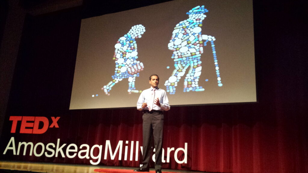Speaker presenting on aging with visual of a young and old person on screen.