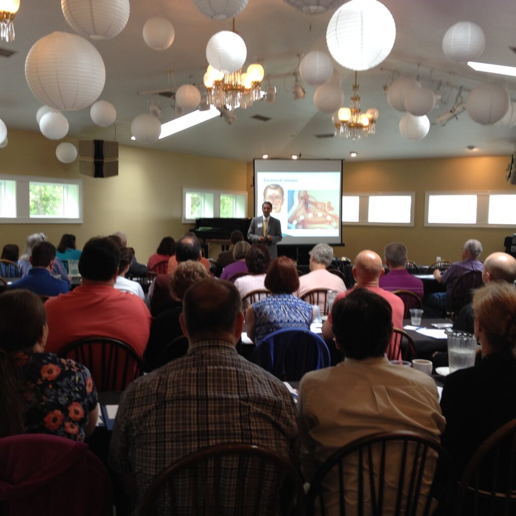 Audience attentively watching a presentation in a conference room with hanging lights.