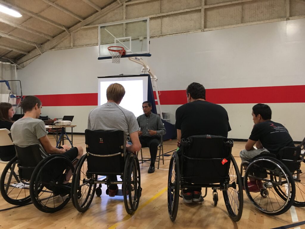 A group in wheelchairs attending a presentation in a gymnasium.